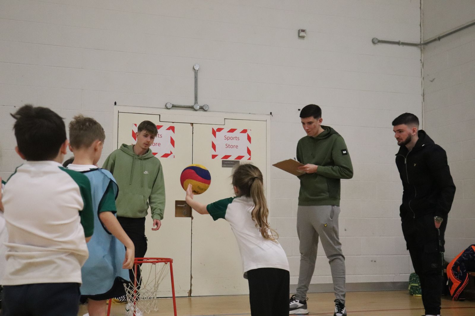 Child throwing ball in a hoop, whilst East Surrey Students support